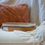 Photo of old books on couch with burnt orange throw pillow