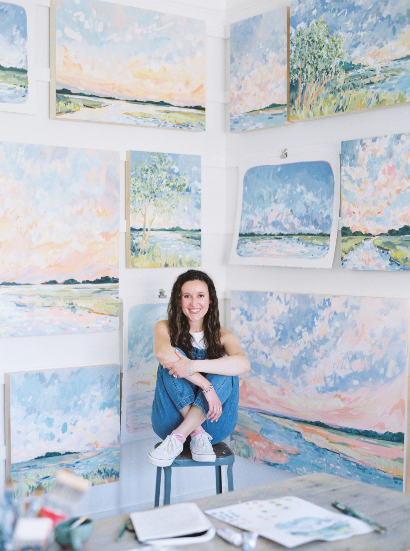 Photo of Sarah Jane Tart in her art studio surrounded by coastal paintings.