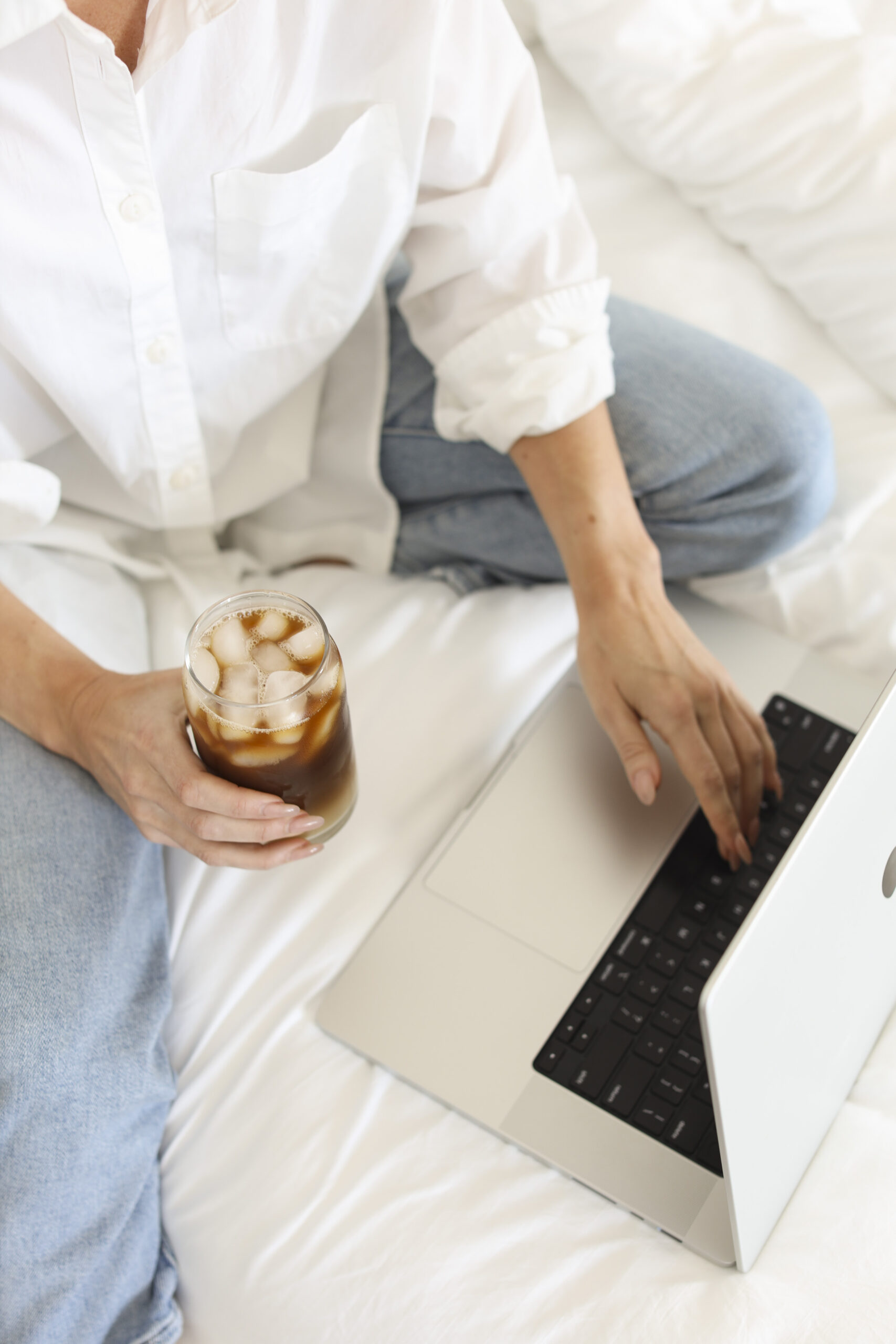 Photo of girl in white button down drinking cold brew and working on computer.